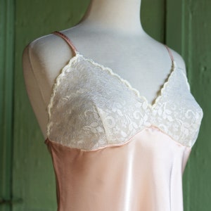 May include: A pale pink satin slip with white lace trim around the neckline. The slip is on a white mannequin.