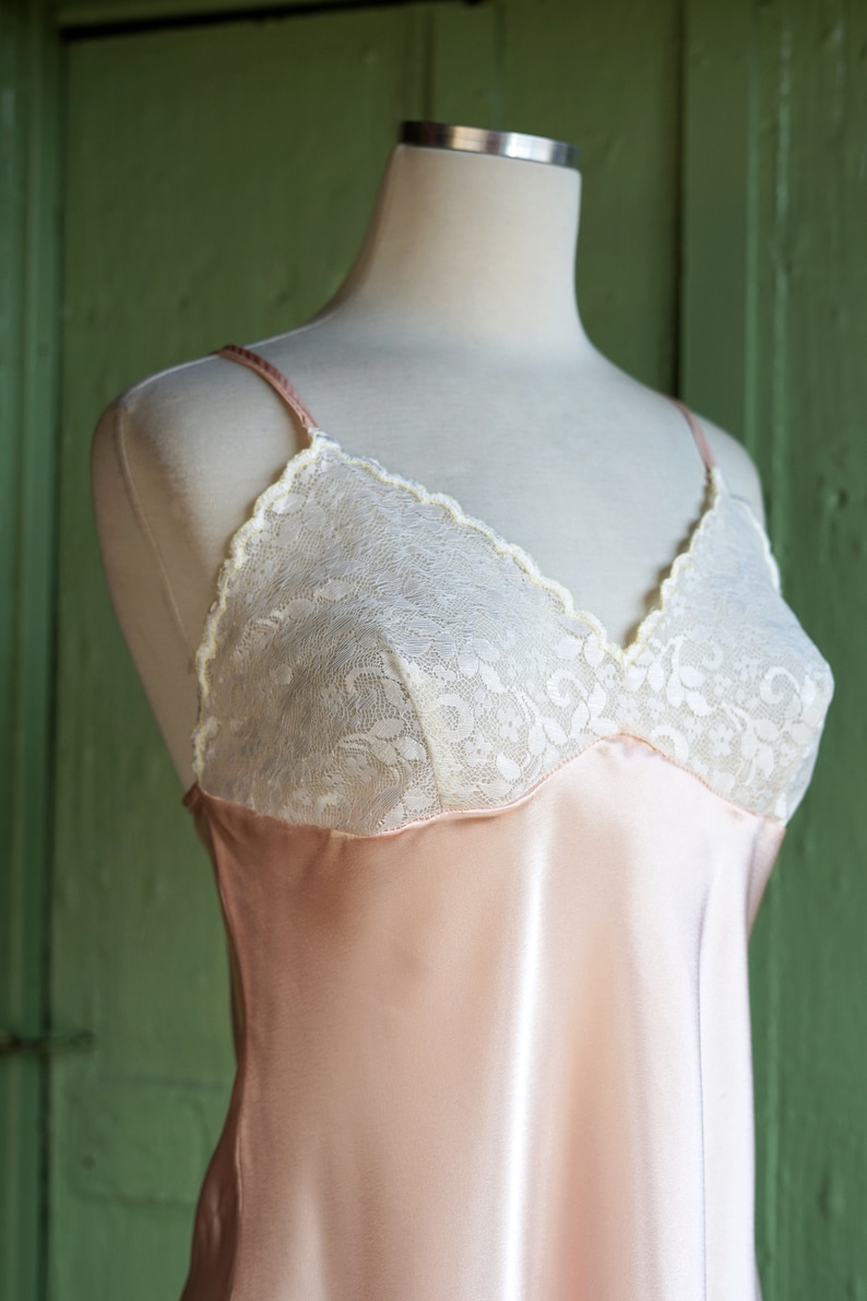 May include: A pale pink satin slip with white lace trim around the neckline. The slip is on a white mannequin.