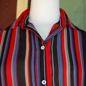 May include: A striped button-down shirt with red, blue, black, and beige stripes. The shirt has a collar and two buttons.