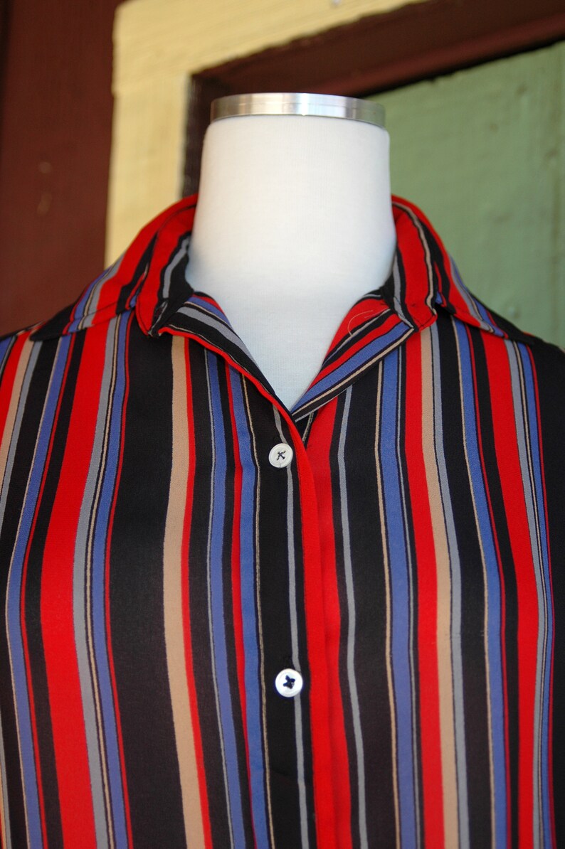 May include: A striped button-down shirt with red, blue, black, and beige stripes. The shirt has a collar and two buttons.