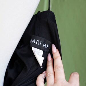May include: A black dress with a white tag that reads "Bari Jay" and "Exclusive of Decoration 31465  Imported".