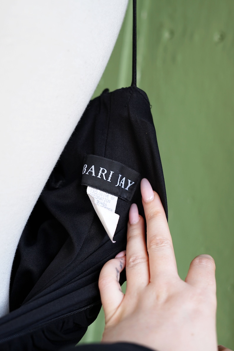 May include: A black dress with a white tag that reads "Bari Jay" and "Exclusive of Decoration 31465  Imported".