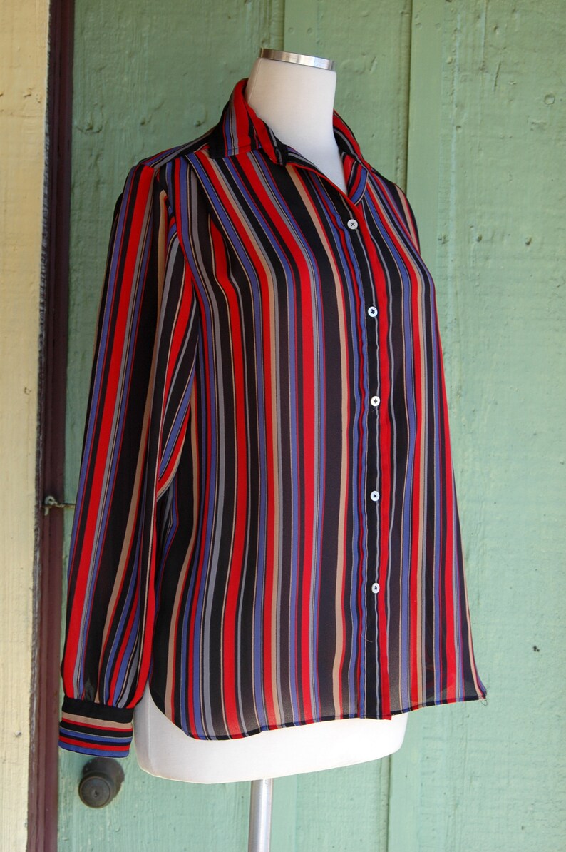 May include: A long-sleeved, striped button-down shirt in black, red, blue, and beige. The shirt is made of a sheer fabric and has a relaxed fit.