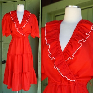 May include: A red vintage dress with a white ruffled neckline and tiered skirt. The dress has a wrap-style bodice and short sleeves.