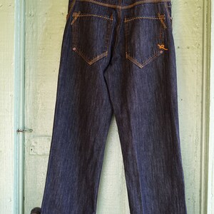 Peut inclure: Un jean en denim bleu fonc&eacute; avec des coutures orange et un petit logo sur la poche arri&egrave;re.