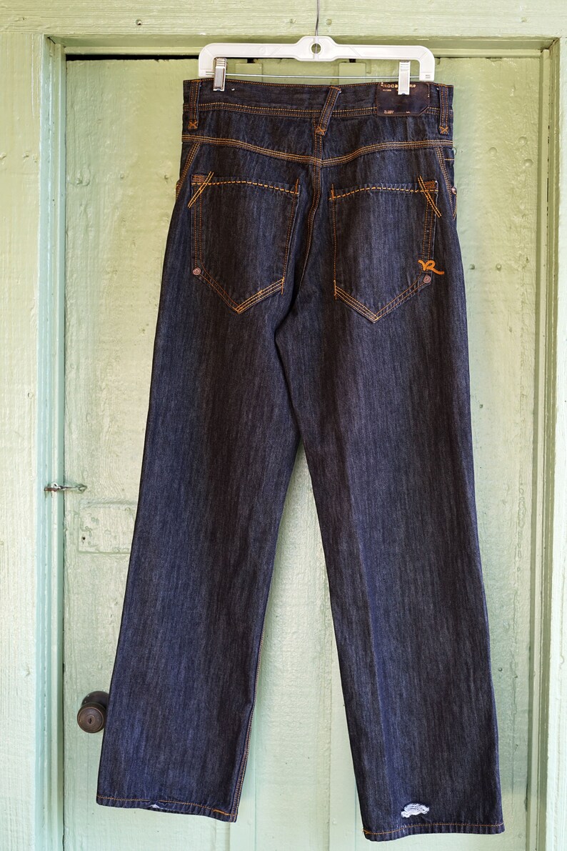 Peut inclure: Un jean en denim bleu fonc&eacute; avec des coutures orange et un petit logo sur la poche arri&egrave;re.