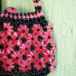 May include: A pink and black beaded purse with a flower design. The purse is hanging on a light green door.
