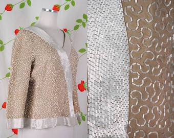 May include: A beige jacket with a silver trim and a delicate pattern. The jacket is made of a soft, textured fabric and has a V-neckline.