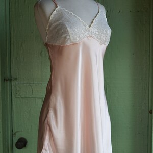 May include: A pink satin slip dress with white lace trim around the neckline.