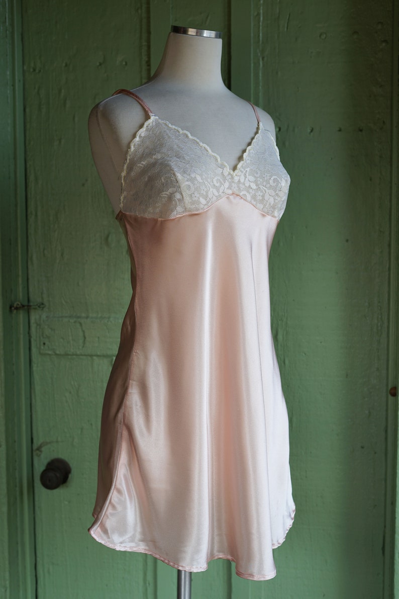 May include: A pink satin slip dress with white lace trim around the neckline.