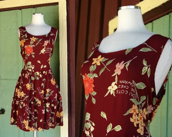 May include: A sleeveless burgundy dress with a floral pattern in shades of yellow, orange, and pink. The dress features a scoop neckline and a tiered skirt. Text on the dress reads "DU COTE CHEZ SWANN".