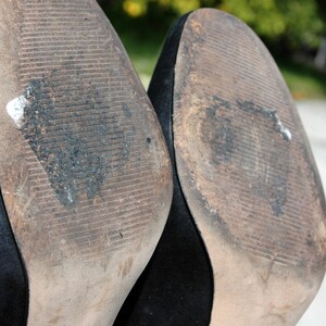 May include: Close-up of the soles of two black high-heeled shoes. The soles are worn and show signs of use, with dirt and wear patterns visible. The brand name "ANN TAYLOR" is visible on the sole.