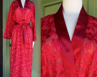 May include: A red satin robe with a floral pattern. The robe has a shawl collar and a tie belt.