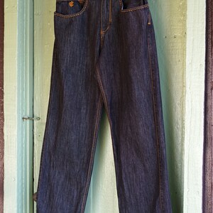 Peut inclure: Un jean en denim bleu fonc&eacute; avec des coutures orange. Le jean porte une &eacute;tiquette de marque qui indique "ROCA WEAR".