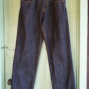 Peut inclure: Un jean en denim bleu fonc&eacute; avec des coutures orange. Le jean a une coupe d&eacute;contract&eacute;e et une jambe droite. Le nom de la marque "ROCA WEAR" est imprim&eacute; sur la ceinture arri&egrave;re.