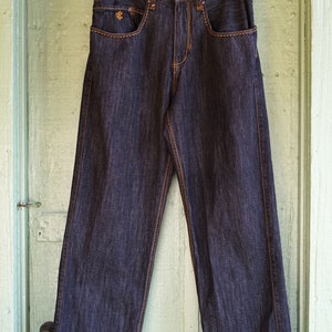 Peut inclure: Un jean en denim bleu fonc&eacute; avec des coutures orange. Le jean a une coupe d&eacute;contract&eacute;e et une jambe droite. Le nom de la marque "ROCSTAR" est imprim&eacute; sur la ceinture arri&egrave;re.
