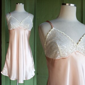 May include: A pale pink satin slip dress with white lace trim around the neckline. The dress has thin adjustable straps.
