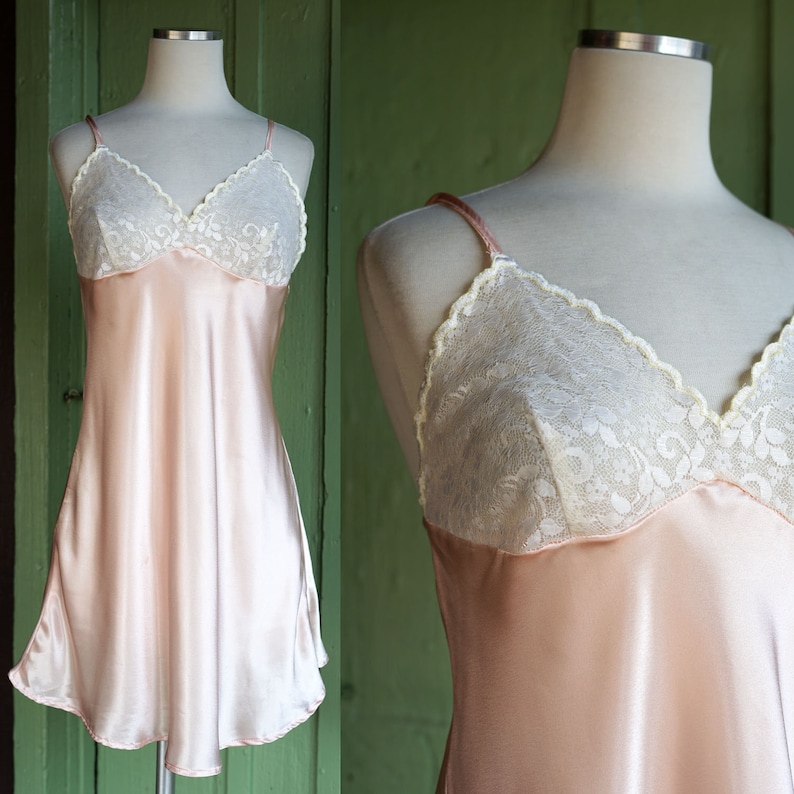 May include: A pale pink satin slip dress with white lace trim around the neckline. The dress has thin adjustable straps.