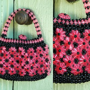 May include: A small pink and black beaded purse with a flower design. The purse has a top handle and is made of plastic beads.