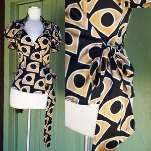 May include: A black and gold wrap top with a geometric pattern. The top has a V-neckline and short puff sleeves. The fabric is silky and has a sheen.
