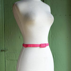 K&ouml;nnte beinhalten: Eine wei&szlig;e Kleiderpuppe mit einem leuchtend pinkfarbenen G&uuml;rtel. Der G&uuml;rtel hat eine rechteckige Schnalle.
