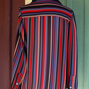 May include: A long-sleeved, striped shirt with a black, red, blue, and beige color scheme. The shirt has a button-up collar and long sleeves with button cuffs.