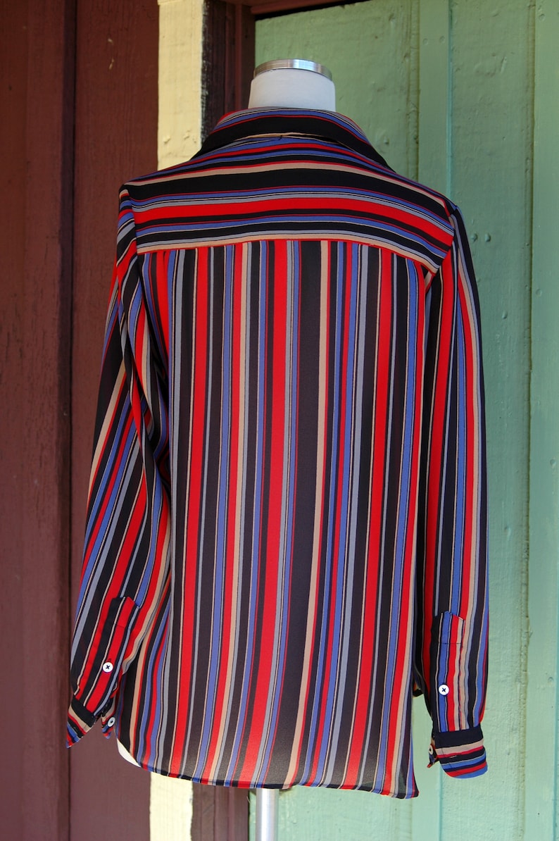 May include: A long-sleeved, striped shirt with a black, red, blue, and beige color scheme. The shirt has a button-up collar and long sleeves with button cuffs.