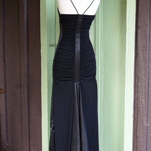 May include: A black, long, sleeveless dress with a fitted bodice and a flowing skirt. The dress has a satin panel down the back.
