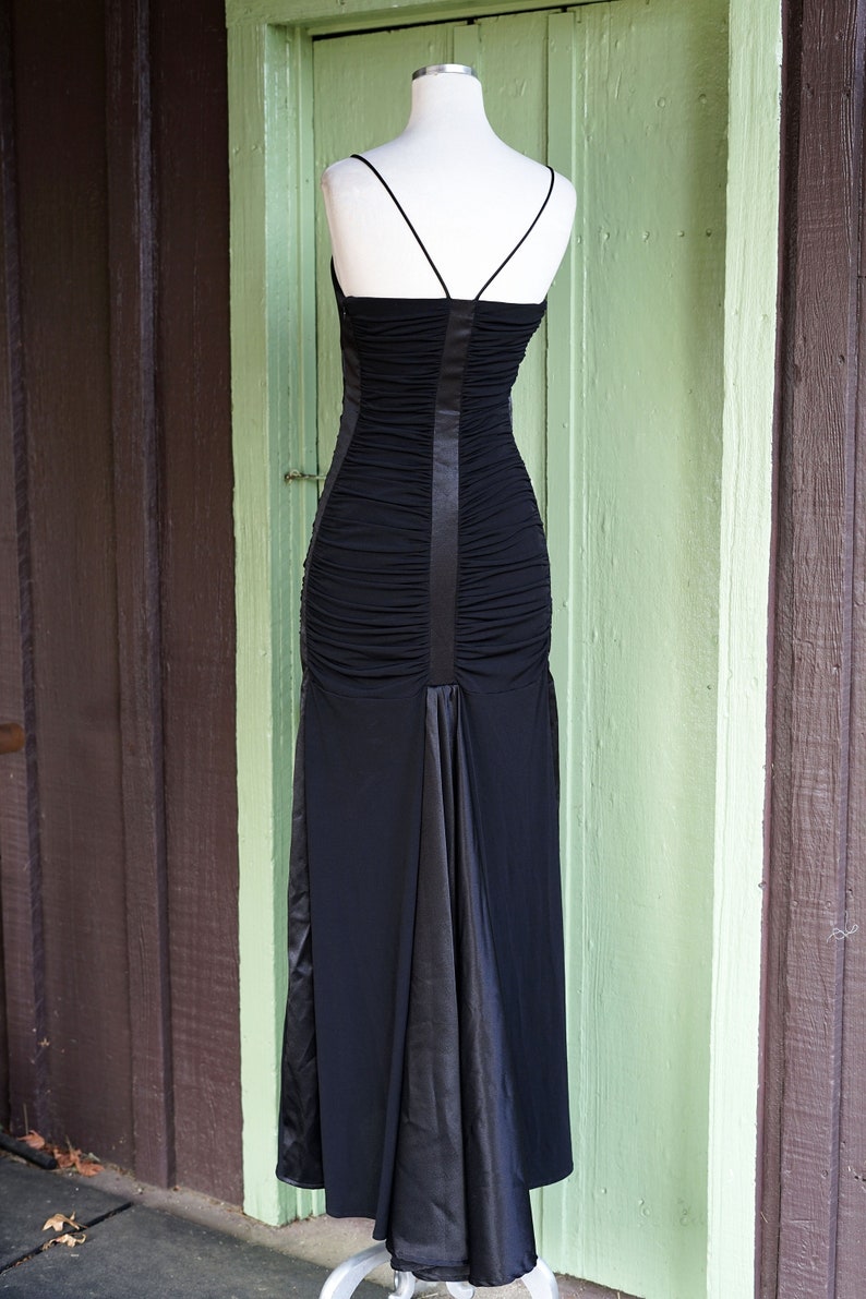 May include: A black, long, sleeveless dress with a fitted bodice and a flowing skirt. The dress has a satin panel down the back.