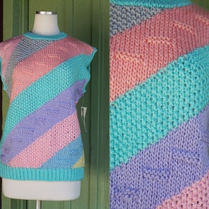 May include: A sleeveless knitted sweater with a diagonal striped pattern in shades of pink, purple, teal, and gray.