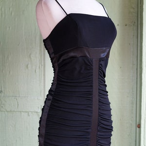 May include: A black, strapless, ruched evening gown with a satin waistband and a fitted silhouette.