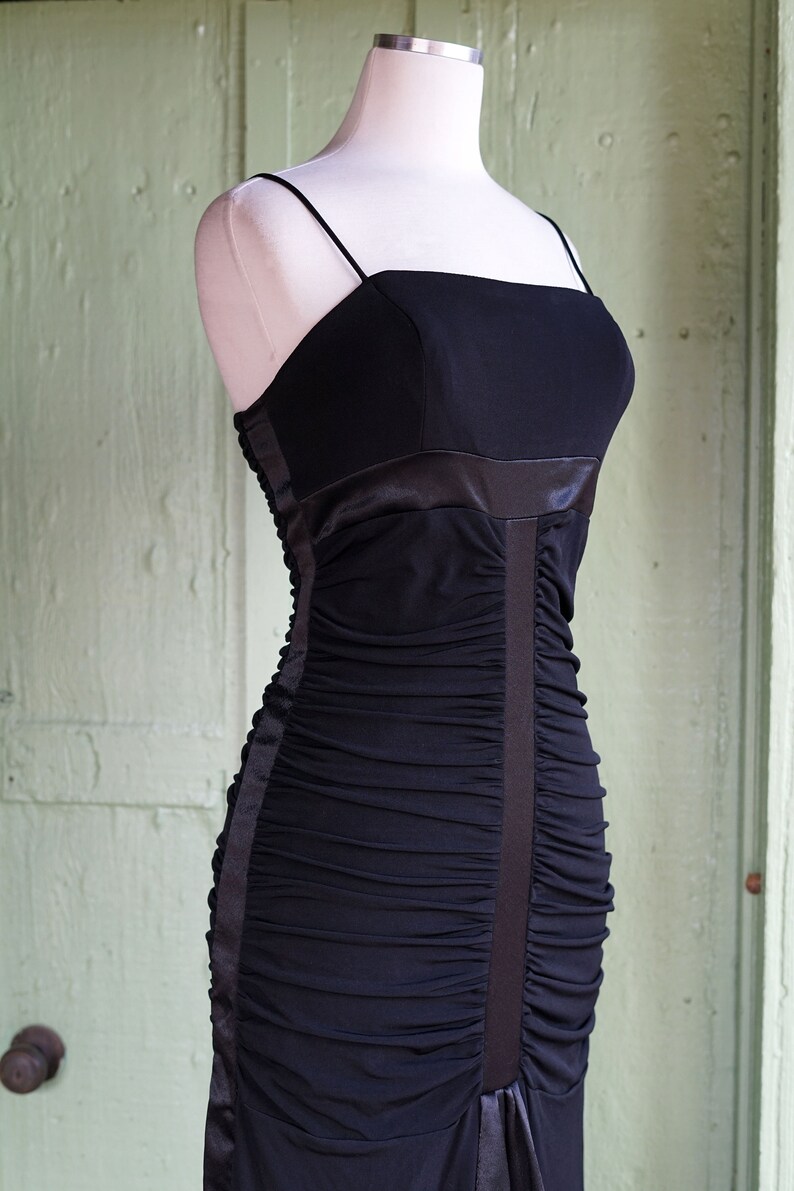 May include: A black, strapless, ruched evening gown with a satin waistband and a fitted silhouette.