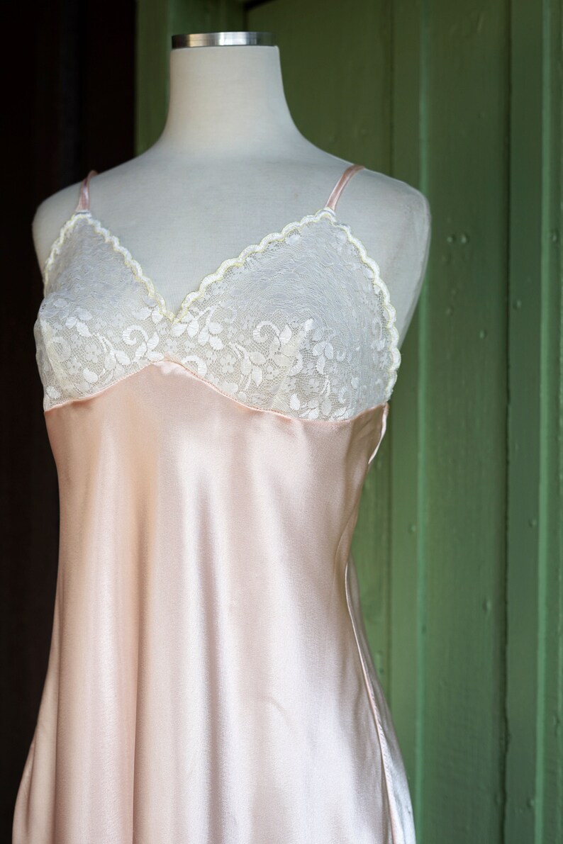 May include: A pale pink satin slip dress with a white lace trim around the neckline.
