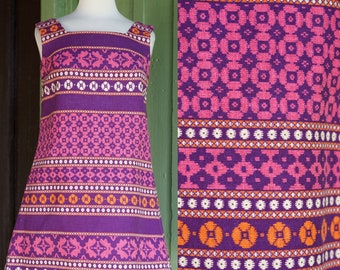 May include: A purple sleeveless mini dress with a geometric pattern in pink, orange, and white. The dress has a square neckline and a straight hem.