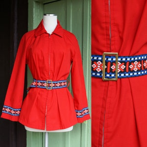 Puede incluir: Chaqueta roja con cremallera con un cintur&oacute;n de estampado geom&eacute;trico y ribetes a juego en los pu&ntilde;os. La chaqueta tiene un cuello cl&aacute;sico y mangas largas.