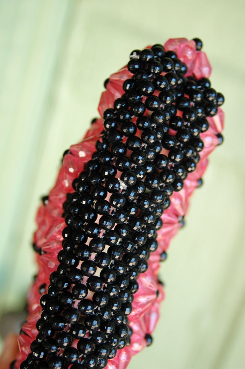 May include: A black and pink beaded necklace with a unique woven design. The beads are small and round, and the necklace is long enough to be worn as a choker or a longer necklace.