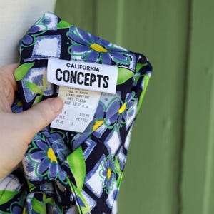 May include: A close-up of a patterned shirt with a floral design in blue, green, and yellow on a navy blue background. The shirt has a white tag that reads "CALIFORNIA CONCEPTS". The shirt is size 3 and made in the U.S.A.