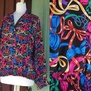 May include: A black button-up blouse with a colorful pattern of bows and ribbons. The fabric has a silky sheen and the blouse has a fitted bodice and long sleeves.
