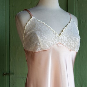 May include: A pale pink satin slip with white lace trim. The slip has a V-neckline and thin straps.
