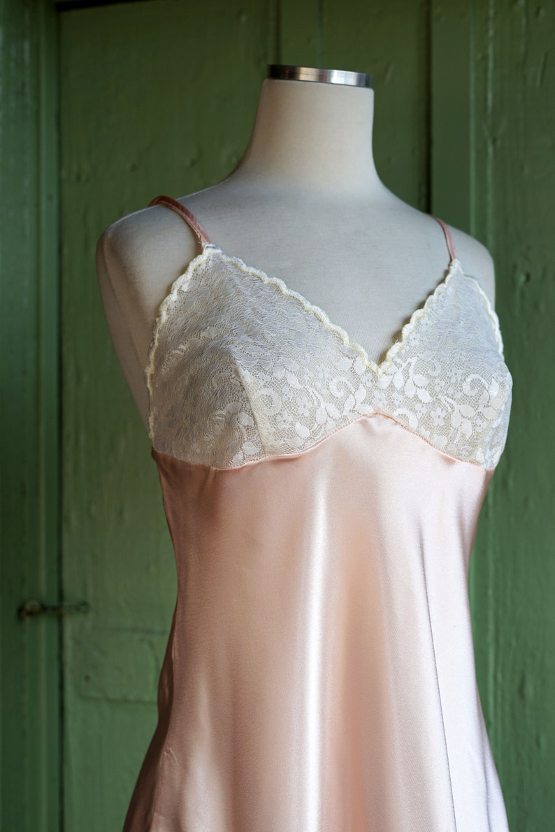 May include: A pale pink satin slip with white lace trim. The slip has a V-neckline and thin straps.