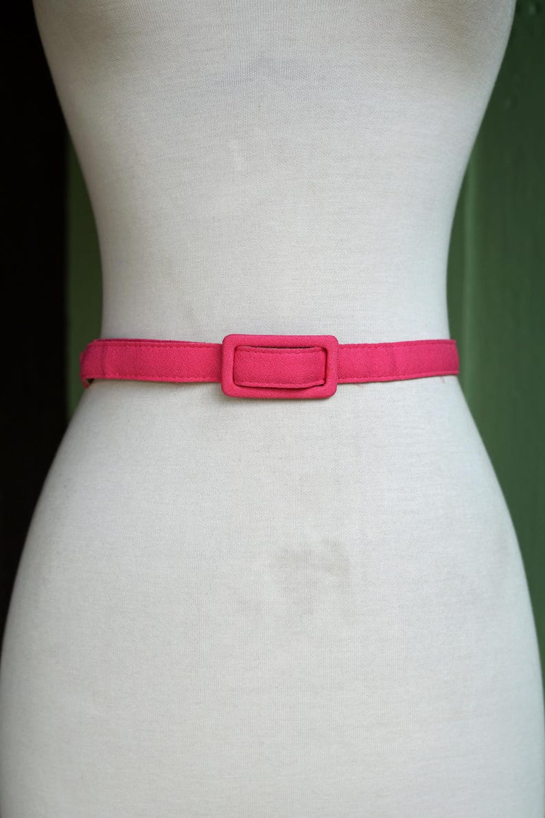 K&ouml;nnte beinhalten: Ein rosa Stoffg&uuml;rtel mit einer rechteckigen Schnalle.