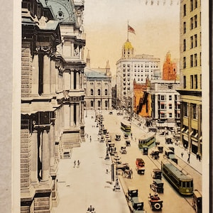 May include: Vintage postcard depicting East City Hall Square in Philadelphia, Pennsylvania. The image shows a bustling street scene with early 20th-century automobiles, trolleys, and horse-drawn carriages. Buildings line the street, and the sky is a pale yellow.
