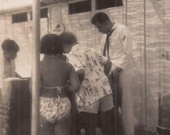 May include: A black and white photo of four people standing in a room. Two people are wearing shirts with patterns, one person is wearing a white shirt, and one person is wearing a patterned swimsuit.