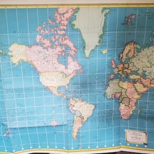 May include: A vintage world map with a blue ocean background and colorful continents. The map shows the world with country borders and labels. The map is folded and has a vintage aesthetic.