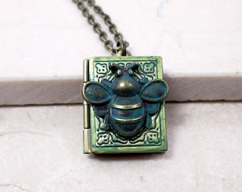 May include: A rectangular, hinged locket necklace with a bronze-colored chain. The locket is green with a raised bee design on the front. The bee and locket have a distressed, antique finish.