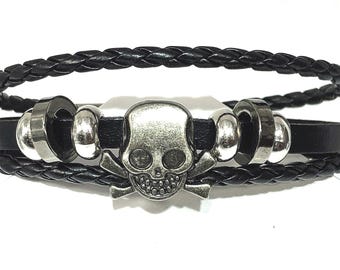 May include: Black leather bracelet with a silver skull charm and silver beads. The bracelet is braided and has a layered design.