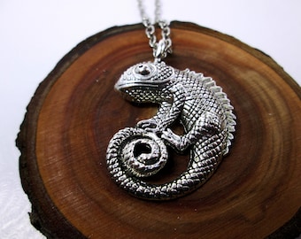 May include: Silver necklace with a detailed chameleon pendant. The chameleon is curled up with its tail wrapped around its body.