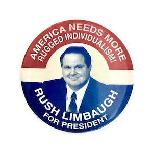 May include: A round button with a portrait of a man in a suit, with the text "America Needs More Rugged Individualism!" in a red and white border. The bottom half reads "Rush Limbaugh For President" in blue.