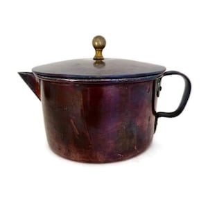 May include: A vintage copper teapot with a lid and handle. The teapot has a dark, iridescent finish with hints of purple and blue. The lid is topped with a small, brass-colored knob. The handle is black.