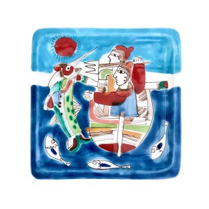 May include: A blue and white ceramic tile with a colorful illustration of two people in a boat with a fish jumping out of the water. The sun is shining in the background.